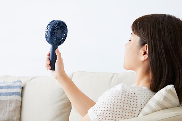 Frau pustet sich mit Handventilator Luft ins Gesicht.