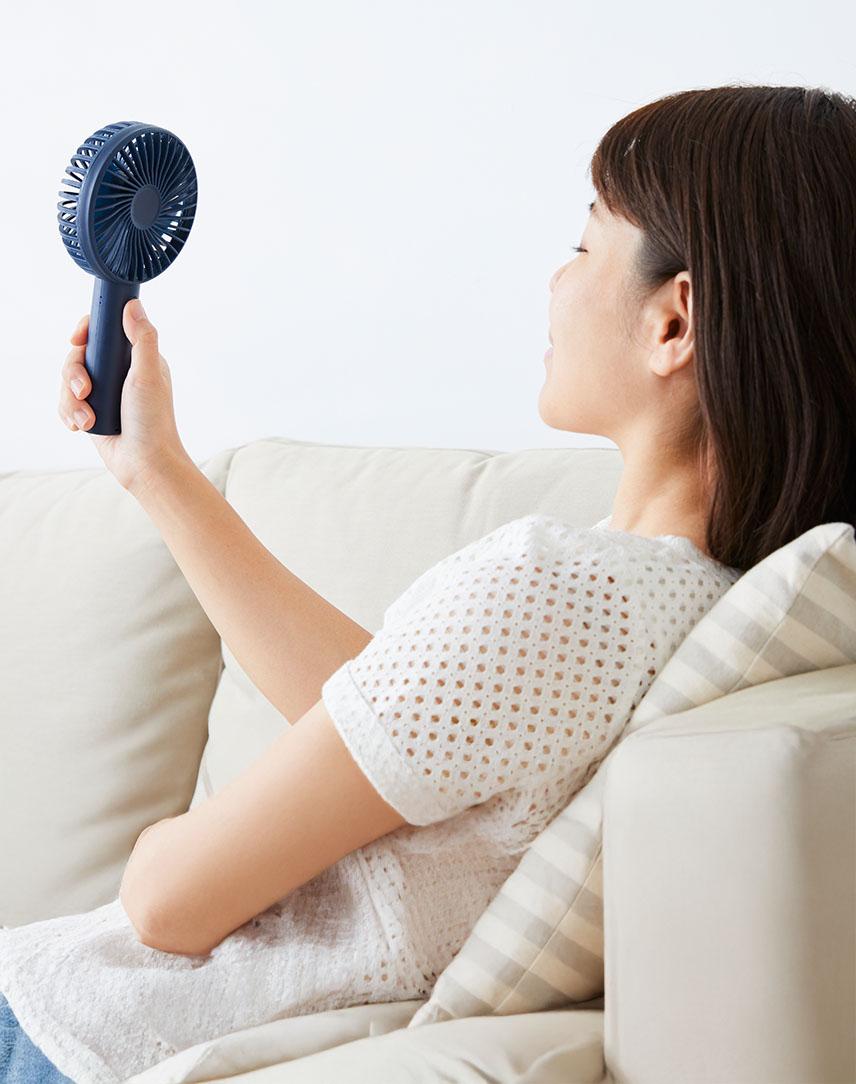 Frau pustet sich mit Handventilator Luft ins Gesicht.