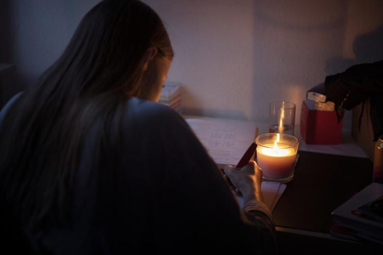 Frau schreibt bei Kerzenlicht in ihrem ansonsten dunklen Zuhause