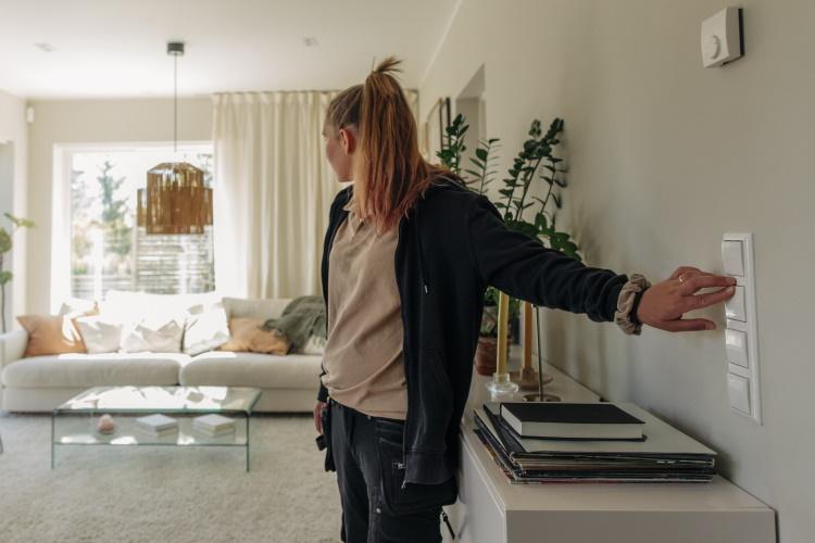 Junge Frau schaltet das Licht in ihrem Wohnzimmer an