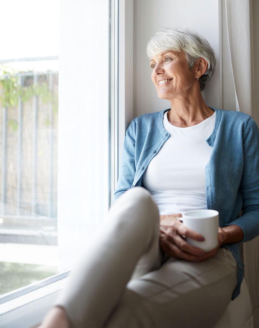 Frau mittleren Alters sitzt auf der Fensterbank und schaut raus