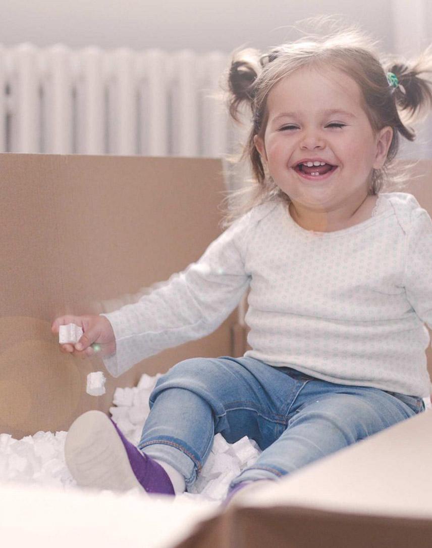 Mädchen sitzt in Umzugskarton vor einer Heizung